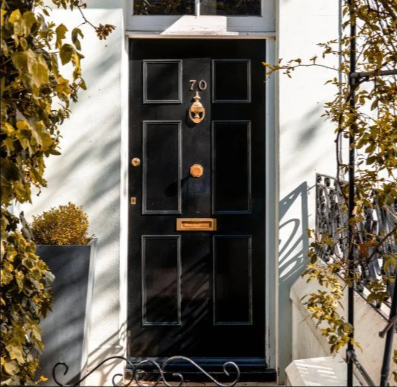 Black front door numbered 70 with brass hardware on white building facade