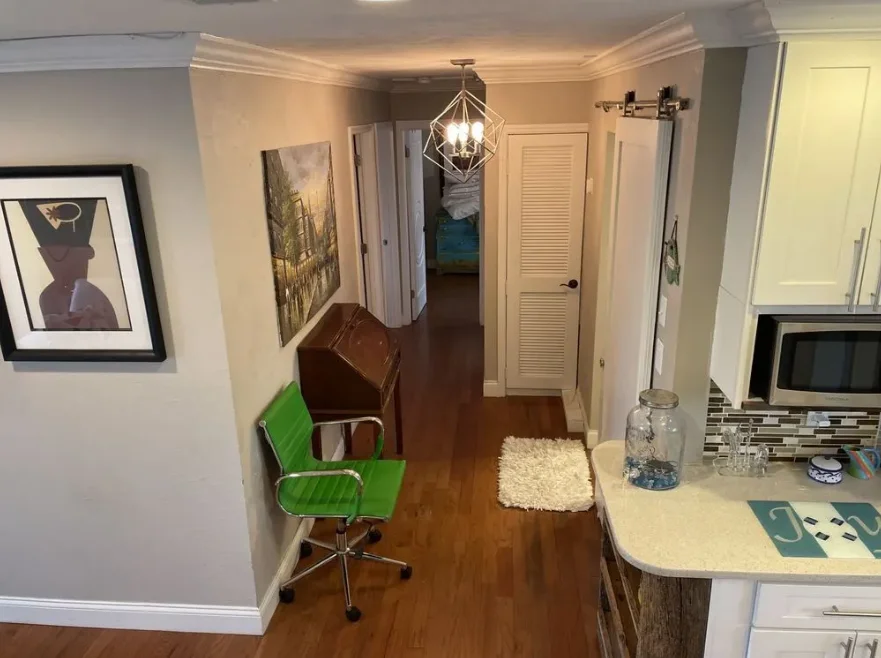 Modern apartment hallway with green office chair, wooden flooring, and kitchen visible on right