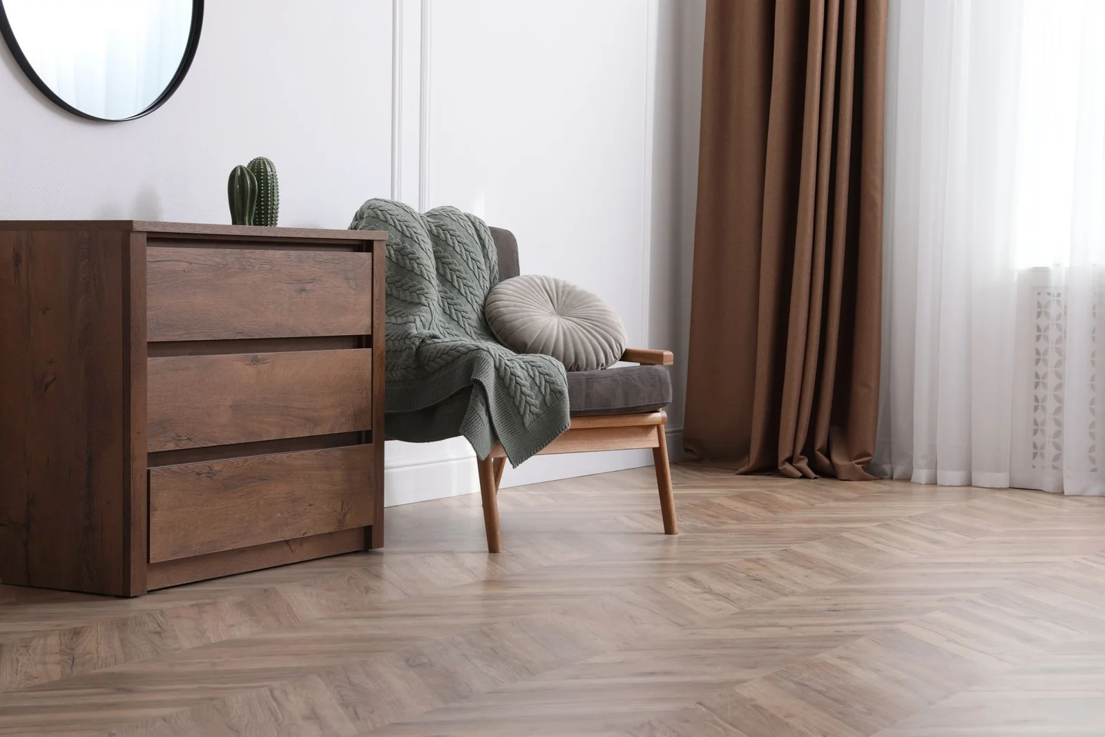 Modern living room with wooden dresser, gray armchair, green throw blanket, and brown curtains