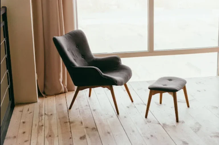 Modern black armchair with wooden legs and matching ottoman in bright room with large windows