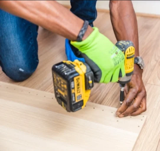 Worker in safety gloves using power drill on wooden flooring