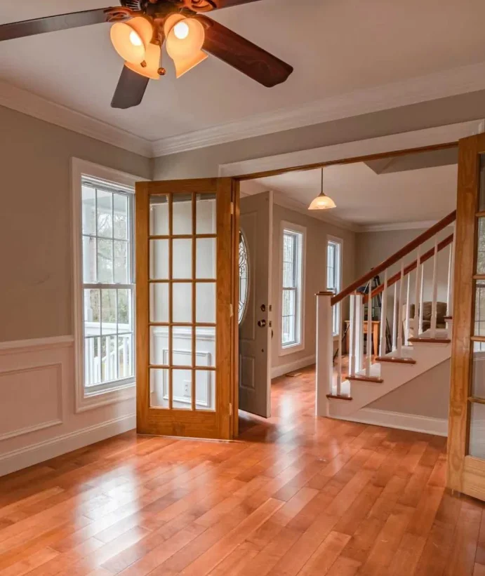 Bright interior foyer with hardwood floors, ceiling fan, wooden French doors, and staircase