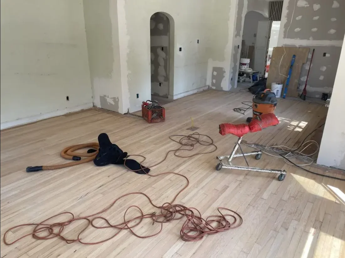 Construction site interior with drywall, wooden flooring, extension cords, and ventilation equipment