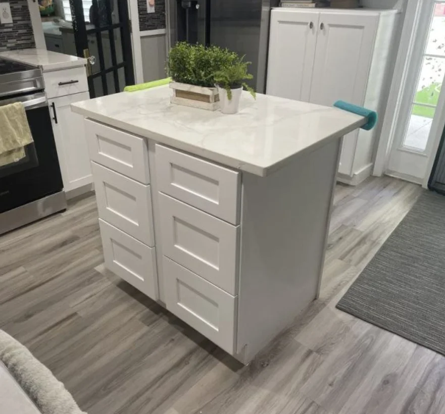 White kitchen island with drawers, white countertop, and potted green plant