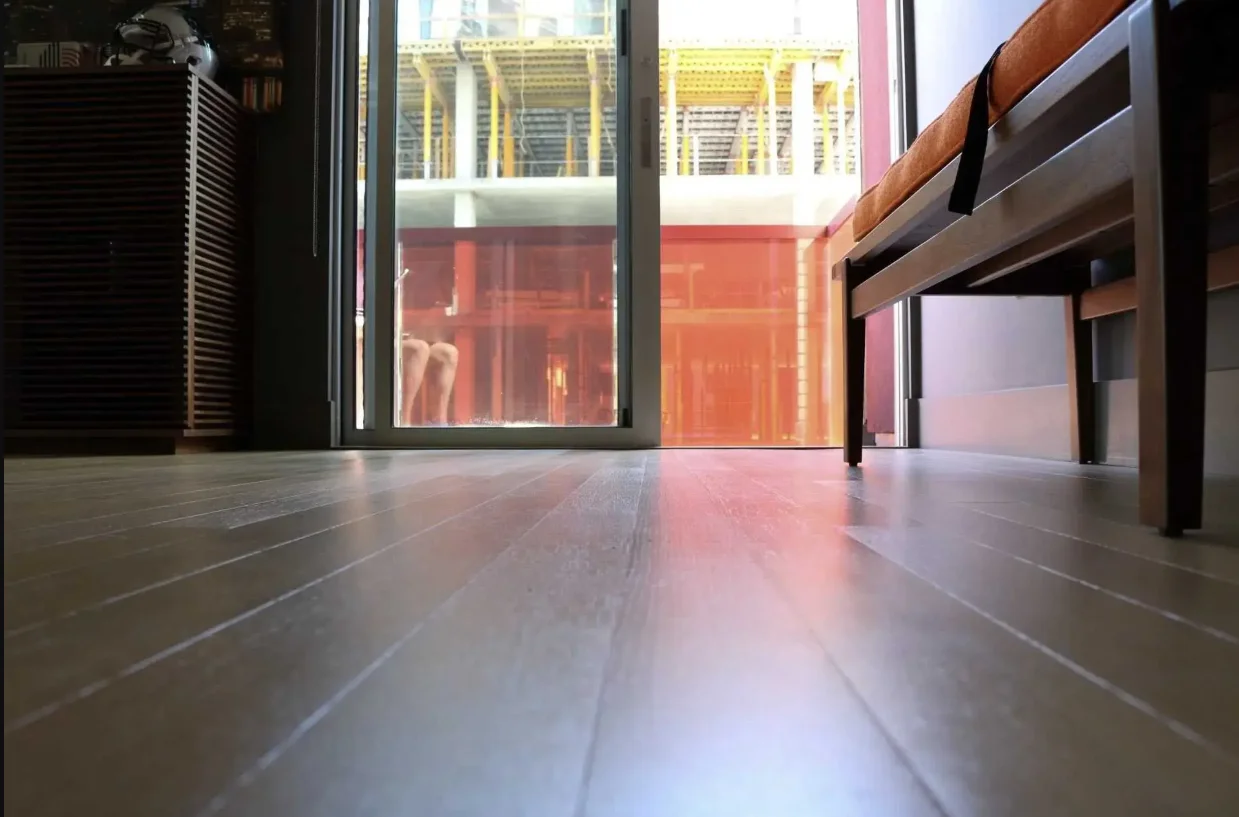 Empty modern office interior with wooden flooring, floor-to-ceiling windows, and built-in shelving