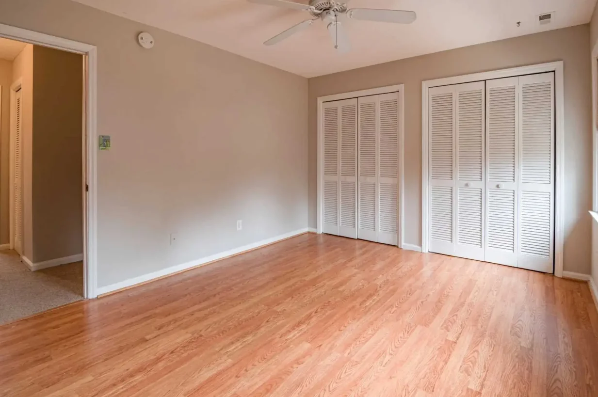 Empty bedroom with hardwood floors, two closets with louvered doors, and beige walls